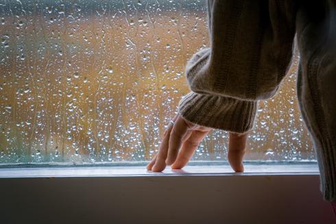 A person is standing in front of a rainy window.