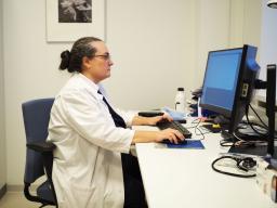 Nainen valkoisessa lääkärintakissa istuu tietokoneen äärellä.